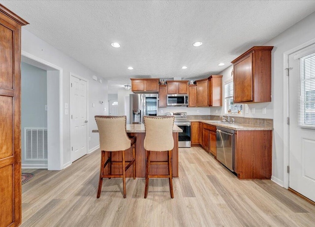 kitchen with appliances with stainless steel finishes, visible vents, a kitchen island, and light wood finished floors