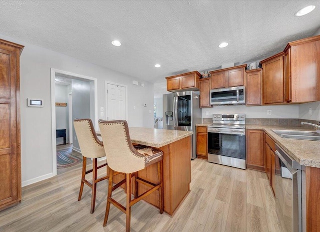 kitchen featuring stainless steel appliances, a sink, light wood-style flooring, and a breakfast bar area