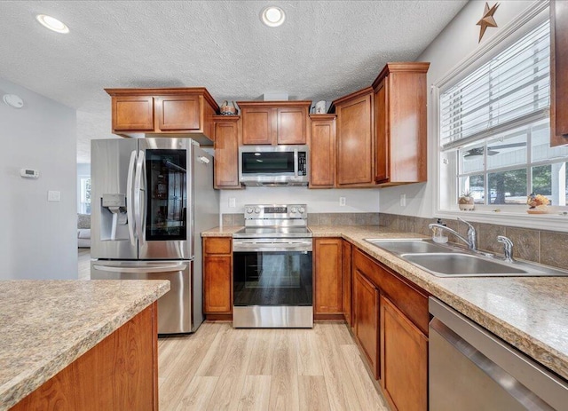 kitchen with stainless steel appliances, light wood-style floors, brown cabinets, and a sink