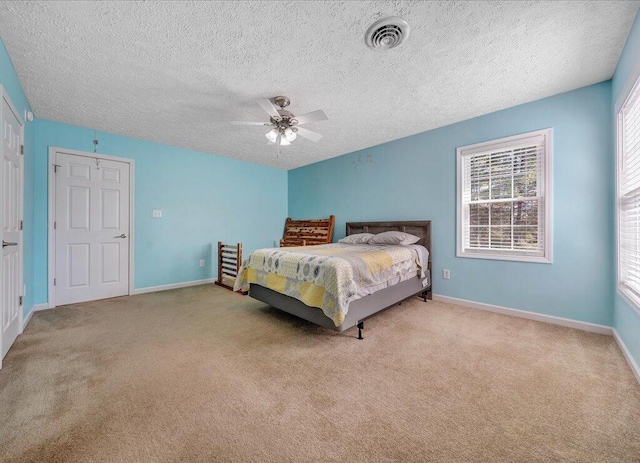 bedroom with a textured ceiling, a ceiling fan, visible vents, baseboards, and carpet