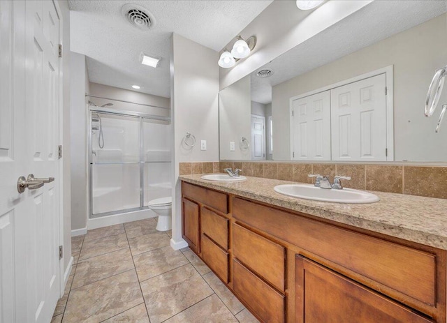 full bath with a textured ceiling, toilet, a sink, visible vents, and a stall shower