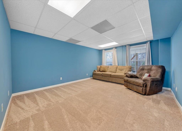 unfurnished living room featuring carpet flooring, a drop ceiling, and baseboards