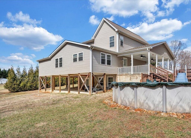 rear view of property featuring stairs, a yard, a ceiling fan, and a covered pool