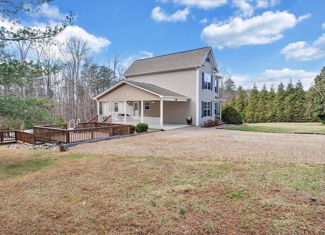 rear view of house with driveway, a lawn, and a wooden deck