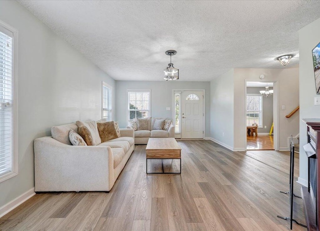 living room with a textured ceiling, a fireplace, baseboards, light wood finished floors, and an inviting chandelier