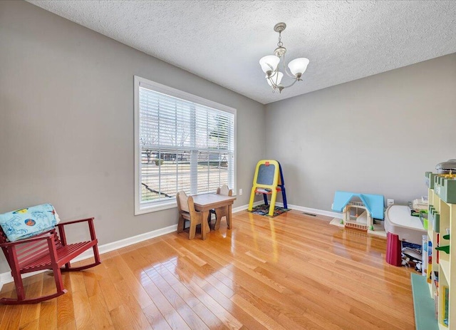 game room with baseboards, light wood finished floors, a textured ceiling, and a notable chandelier