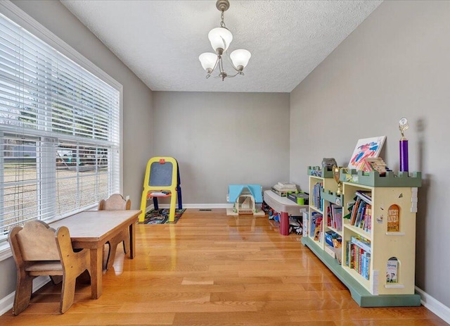 game room with light wood-type flooring, an inviting chandelier, baseboards, and a textured ceiling