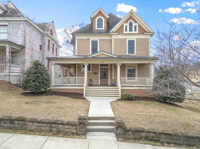 view of front of property with a front lawn, covered porch, and a shingled roof