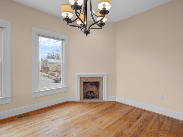 unfurnished living room featuring wood finished floors, visible vents, baseboards, a fireplace, and a chandelier