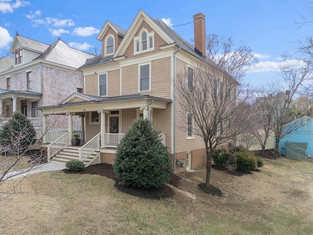 traditional style home featuring a porch, a chimney, and a front lawn