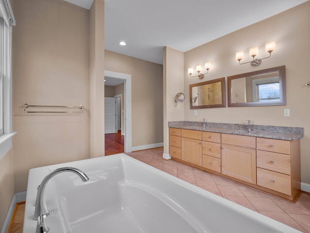 bathroom featuring a tub to relax in, a sink, tile patterned flooring, double vanity, and baseboards