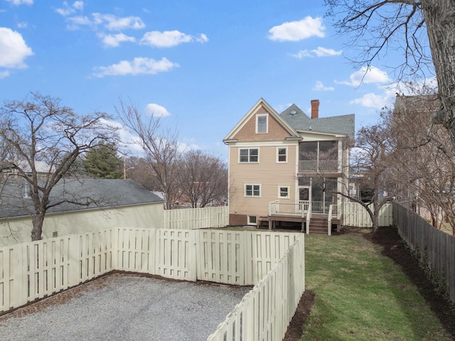 back of property with a fenced front yard, a wooden deck, a chimney, a yard, and a sunroom