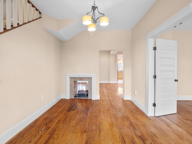 unfurnished living room with an inviting chandelier, wood finished floors, a fireplace, and baseboards