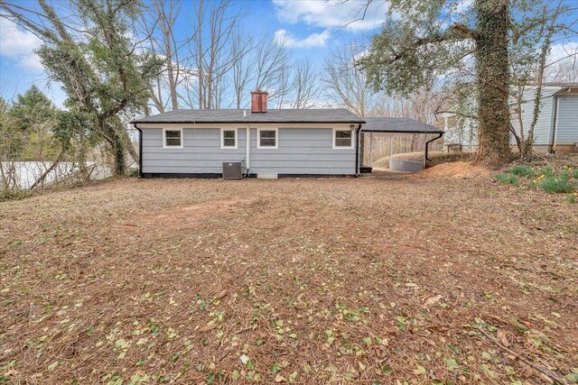 rear view of house with an attached carport, central air condition unit, fence, and a chimney