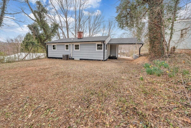 back of property featuring an attached carport, central AC, and a chimney