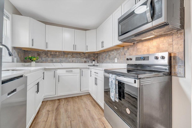 kitchen with a sink, white cabinets, backsplash, and stainless steel appliances