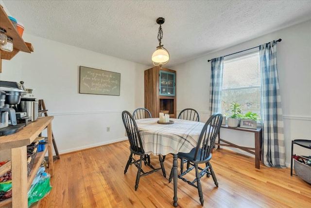 dining room featuring light wood-style floors, baseboards, and a textured ceiling