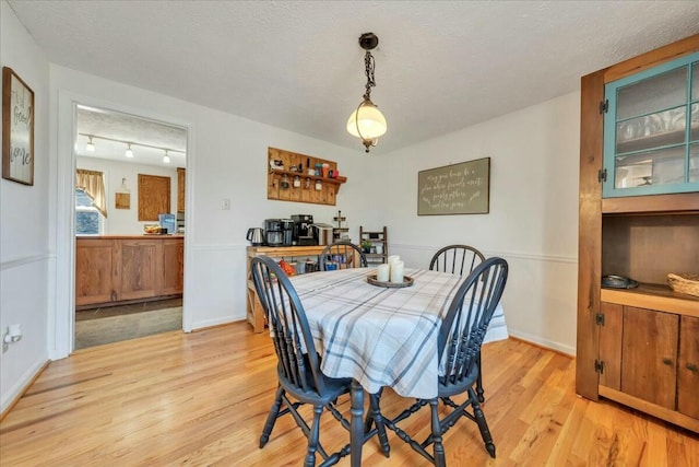 dining space with baseboards, a textured ceiling, and light wood finished floors