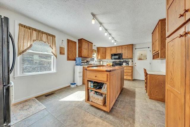 kitchen with baseboards, a kitchen island, a textured ceiling, black appliances, and wooden counters