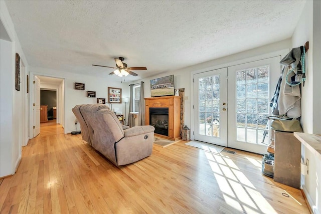 living area with light wood-type flooring, french doors, a fireplace with raised hearth, and a textured ceiling