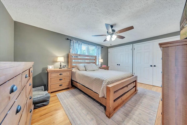 bedroom featuring a textured ceiling, multiple closets, a ceiling fan, and light wood-style floors