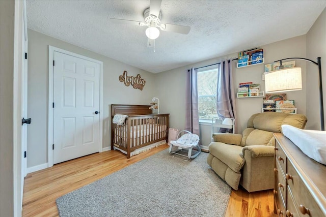 bedroom with light wood-style floors, a nursery area, a textured ceiling, and a ceiling fan