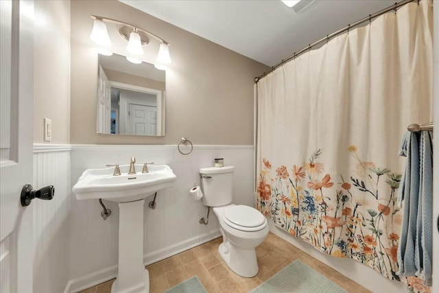 full bath with a wainscoted wall, toilet, a sink, a shower with curtain, and tile patterned floors