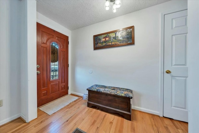 entryway with a textured ceiling, light wood finished floors, and baseboards