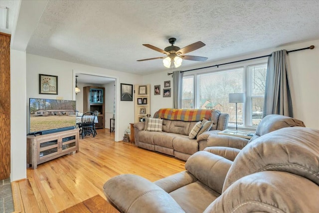 living area with a ceiling fan, a textured ceiling, and light wood finished floors