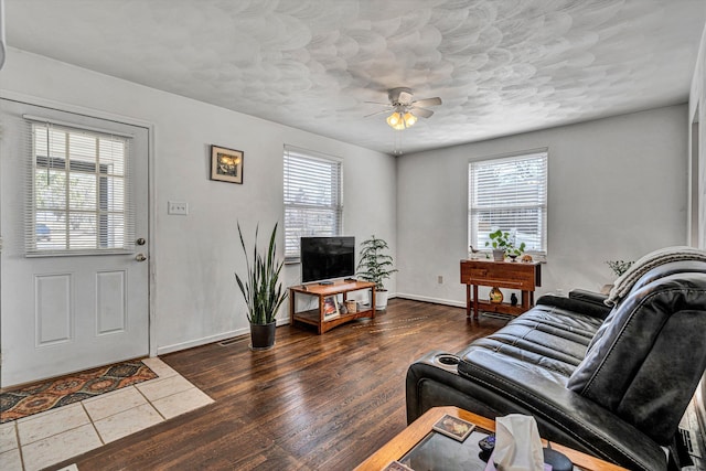 living area with dark wood-style floors, ceiling fan, baseboards, and a wealth of natural light