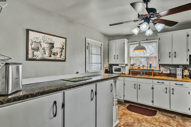 kitchen featuring white microwave, dark countertops, a ceiling fan, and white cabinets