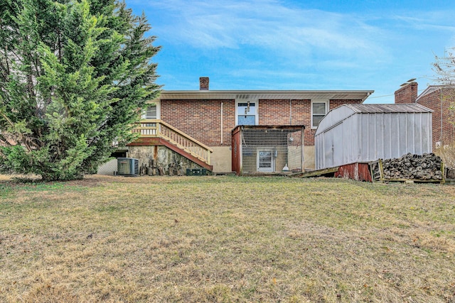 back of house with brick siding, a chimney, central air condition unit, a lawn, and stairs