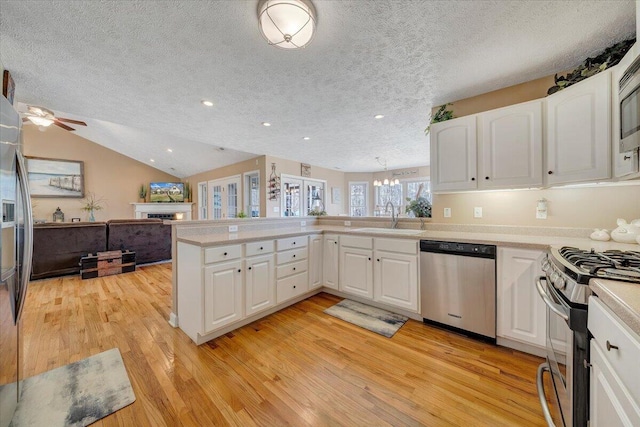 kitchen featuring a sink, appliances with stainless steel finishes, a peninsula, light countertops, and vaulted ceiling