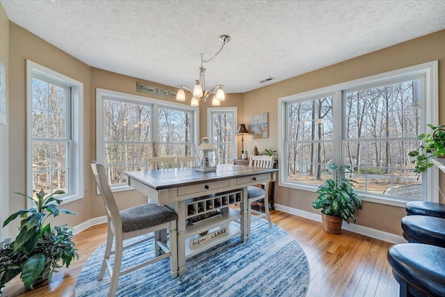 dining space featuring a notable chandelier, baseboards, visible vents, and light wood finished floors