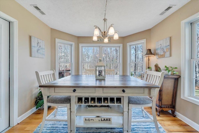 dining space featuring a textured ceiling, light wood-style floors, visible vents, and a chandelier