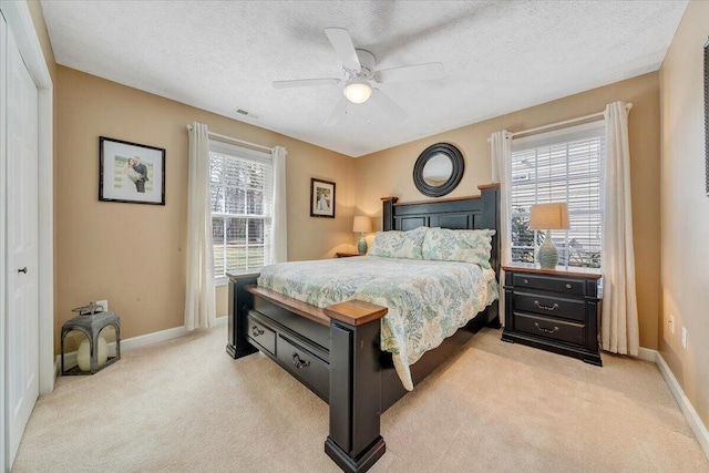 bedroom with a textured ceiling, multiple windows, baseboards, and light carpet