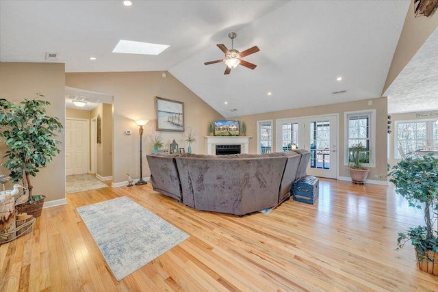 living room with a ceiling fan, baseboards, a fireplace, lofted ceiling with skylight, and light wood-type flooring