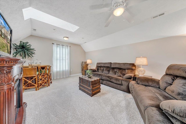 carpeted living area with visible vents, a textured ceiling, vaulted ceiling with skylight, baseboards, and ceiling fan