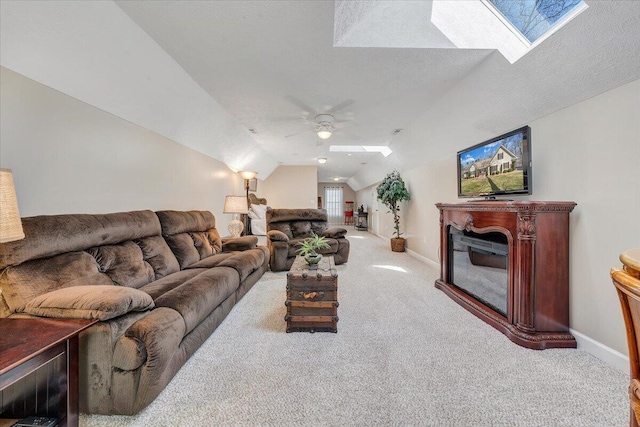 carpeted living area with a ceiling fan, lofted ceiling with skylight, a fireplace, and baseboards