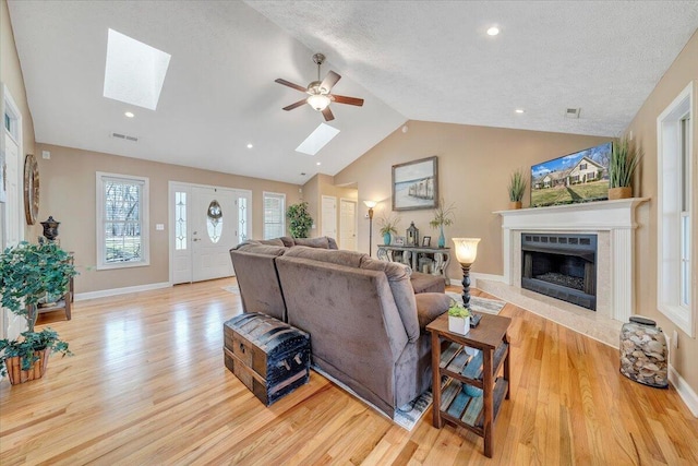 living room featuring wood finished floors, vaulted ceiling with skylight, ceiling fan, and a high end fireplace