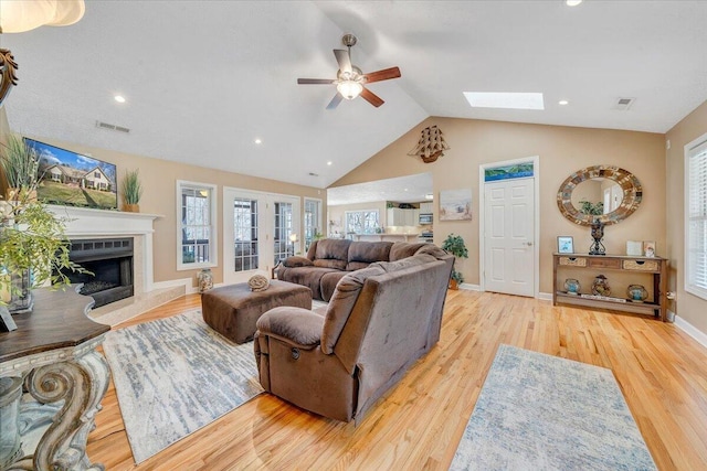 living room with wood finished floors, vaulted ceiling with skylight, a ceiling fan, and visible vents