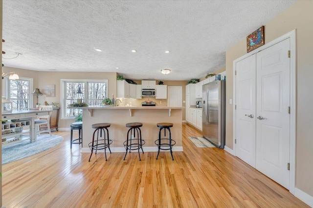 kitchen featuring white cabinetry, a kitchen breakfast bar, stainless steel appliances, and light wood-style floors