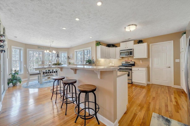 kitchen with stainless steel appliances, light countertops, white cabinets, a kitchen breakfast bar, and light wood-type flooring