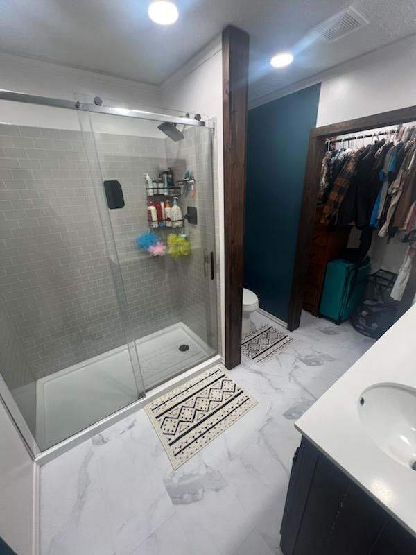 bathroom featuring vanity, visible vents, a shower stall, toilet, and marble finish floor