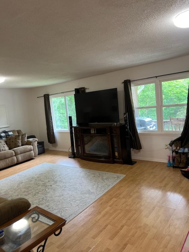 living room with a fireplace, a textured ceiling, baseboards, and wood finished floors