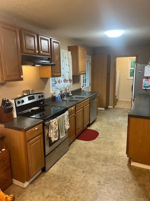 kitchen featuring a sink, dark countertops, appliances with stainless steel finishes, exhaust hood, and brown cabinetry