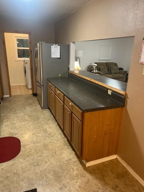 kitchen with brown cabinetry, washer / clothes dryer, freestanding refrigerator, vaulted ceiling, and dark countertops