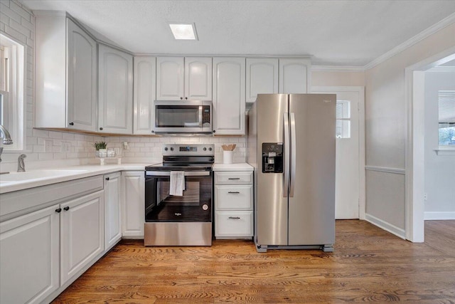 kitchen with light wood-style flooring, ornamental molding, a sink, backsplash, and appliances with stainless steel finishes