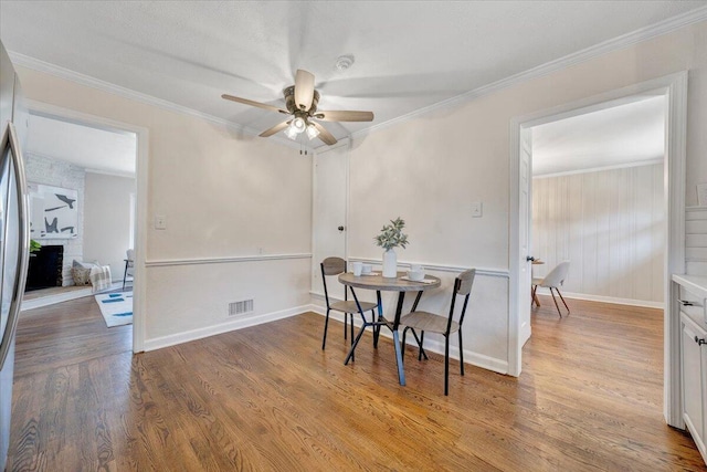 dining room with visible vents, a brick fireplace, crown molding, wood finished floors, and a ceiling fan