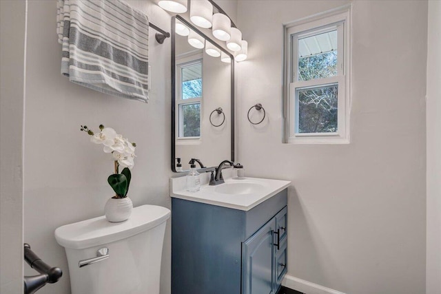 half bath with baseboards, toilet, and vanity